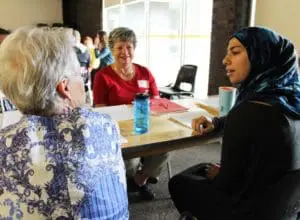A young woman has an interesting discussion with two older women. All are seated at a table.